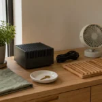 木製サイドボードに放熱を思わせる金属ブロックと小型ファン、電源ケーブル、植物を置き、AIと電力効率の関係を表現した静かな室内写真